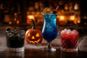 Tres cócteles de Halloween (negro, azul y rojo) con calabaza iluminada y humo sobre barra de madera